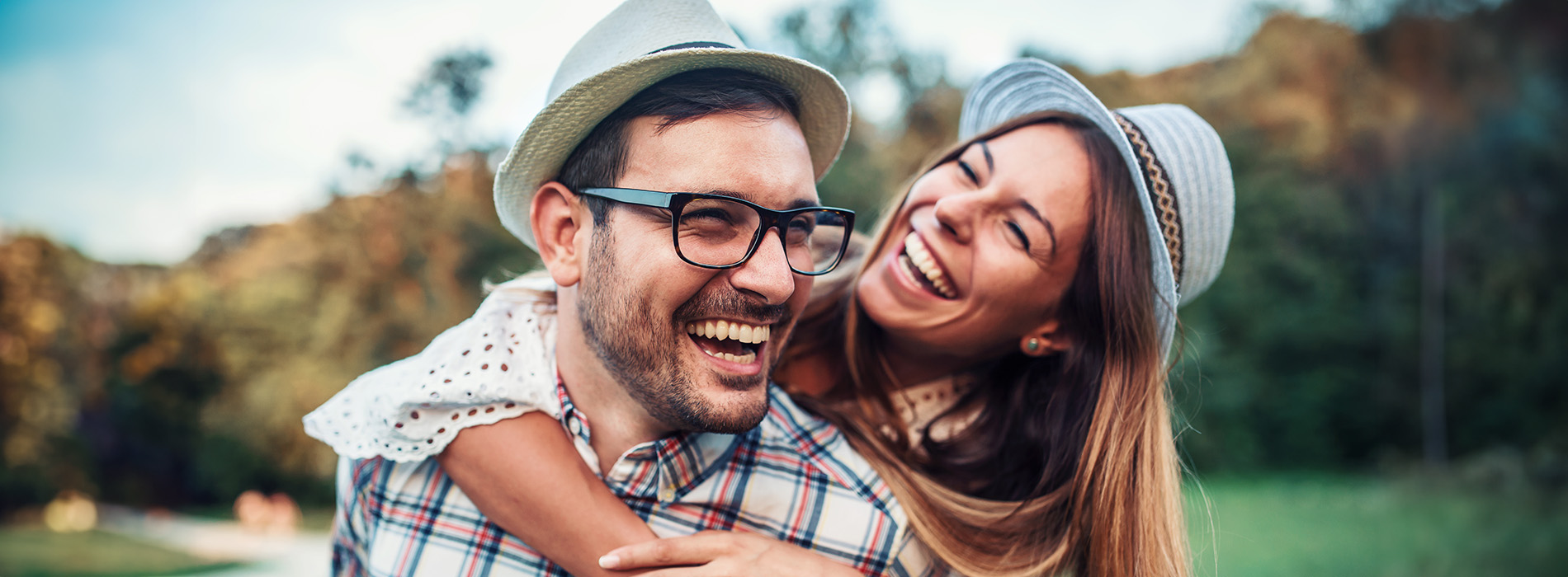 A man and woman are hugging each other outdoors, smiling at the camera  they appear to be a couple enjoying a pleasant moment together.