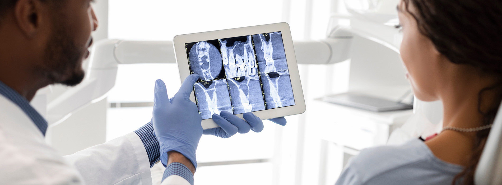 A medical professional using a tablet to display X-rays while a patient looks on with interest.