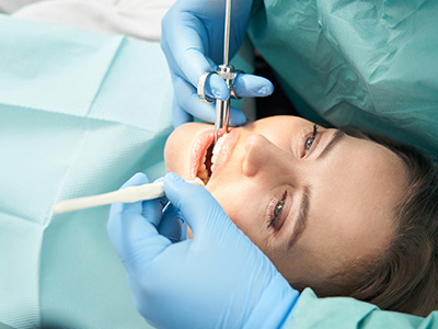The image shows a person receiving dental care with a dental drill being used by a dentist, who is wearing blue gloves and a surgical mask.