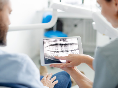 A dental professional shows a patient an X-ray of their teeth on a tablet.