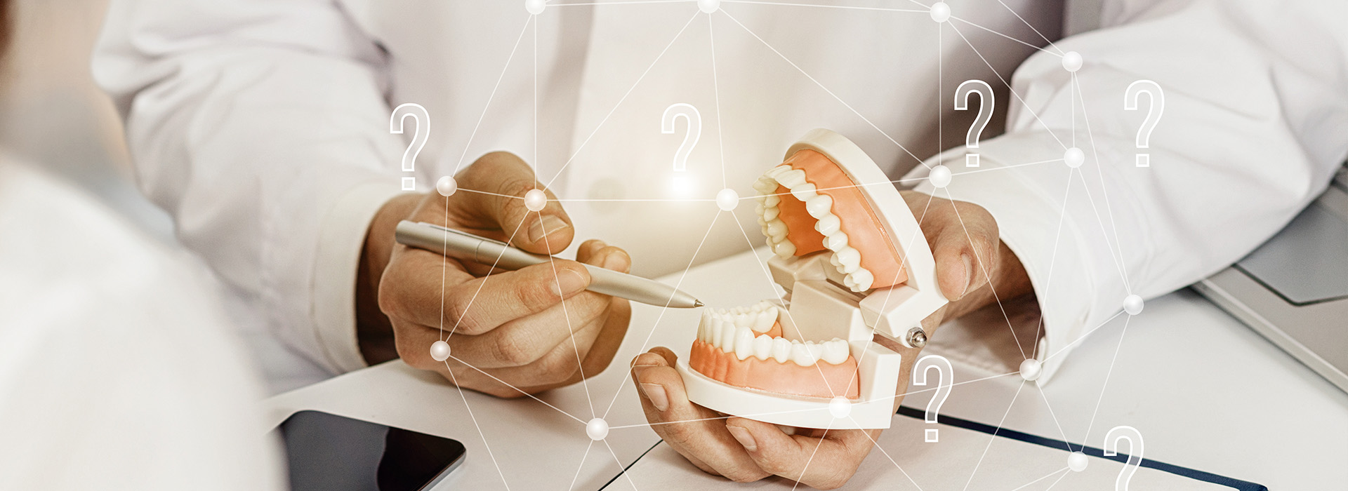 The image shows a human hand holding a set of dentures with teeth visible against a blurred background featuring a computer screen displaying a digital interface with various icons, a person s face partially visible on the left side of the frame, and a blurred figure on the right that appears to be seated at a desk. The overall style of the image is a composite or collage-like presentation combining photography with graphic elements.