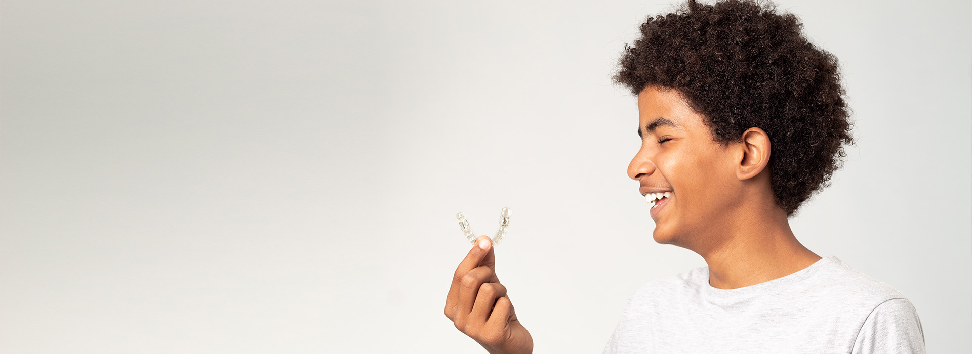 A young adult holding a single flower with a smile, against a plain background.