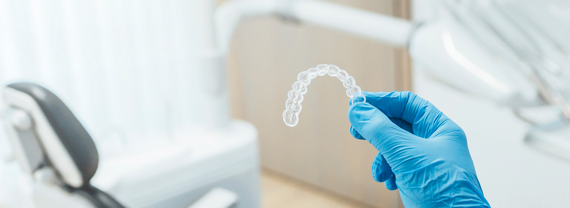 A hand holding a transparent dental implant over a sterile setting with medical equipment.
