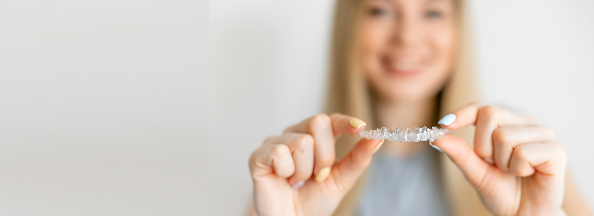 A person holding a small object, possibly jewelry or an award, with a smiling expression against a blurred background.