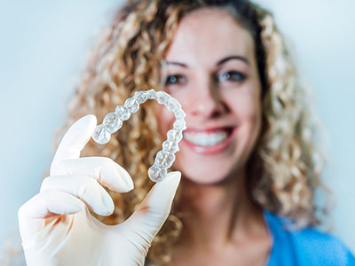 A woman holding up a transparent dental retainer with a smile.