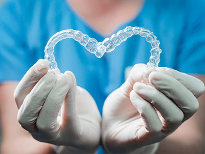 The image shows a person wearing gloves holding a heart-shaped dental implant.