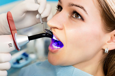 A woman receiving dental treatment under a dental mirror with blue light illumination.