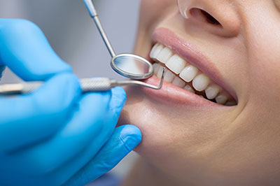 A person receiving dental care with their mouth open, while another person adjusts their teeth using dental instruments.