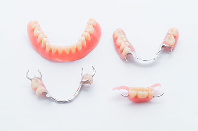 The image shows a set of dentures displayed on a white background, with a focus on the lower teeth section featuring a pink gumline and artificial teeth with a slight smile.
