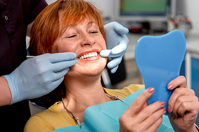 The image shows a woman seated in a dental chair with a blue mouthguard, receiving dental care from a professional who appears to be adjusting her teeth alignment using a dental tool.