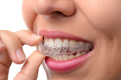 The image shows a person with their hand to their mouth, holding an object that appears to be a toothbrush with bristles.
