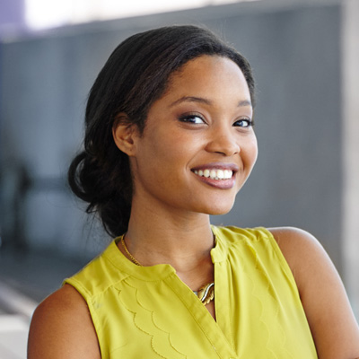 A woman with a radiant smile poses confidently against a wall, her hands casually tucked into her pockets.