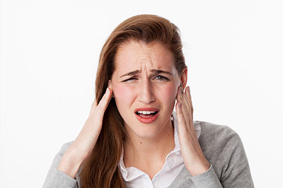 The image shows a woman with her hand on her head, appearing to be in distress or discomfort, possibly due to noise or pain.