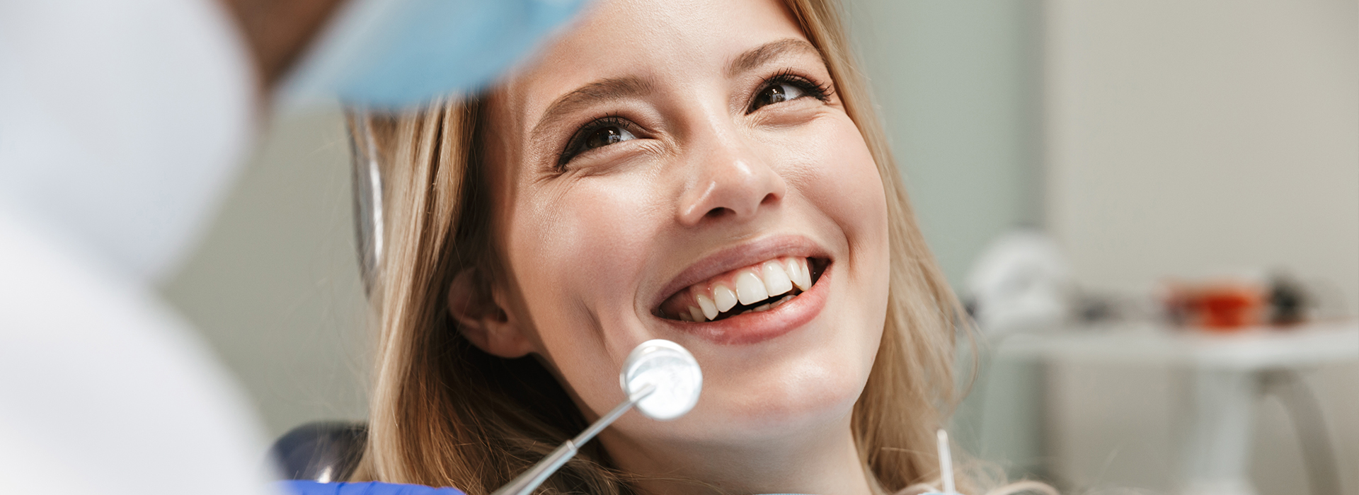 The image depicts a person with a smile, seated in front of a dental professional who appears to be examining their teeth, with a focus on oral hygiene.