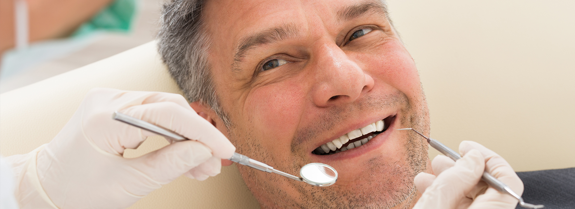 A smiling man sitting in a dental chair with his mouth open while receiving dental care from a dentist.