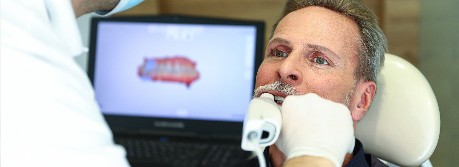 A man receiving dental treatment, with a dentist performing a procedure using a computerized system.