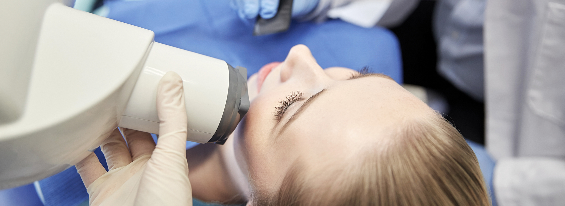 A woman receiving dental treatment with a dentist using a magnifying glass for examination.