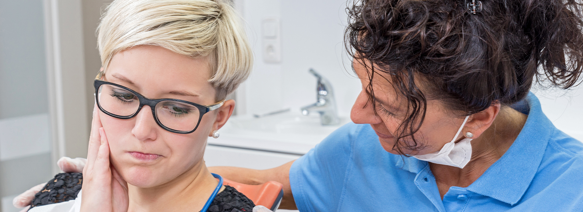 The image shows a woman receiving dental care from another woman, with both individuals wearing masks and glasses, set against an indoor background.