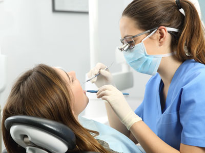 Woman receiving dental care from a female dentist wearing blue gloves and a face mask.