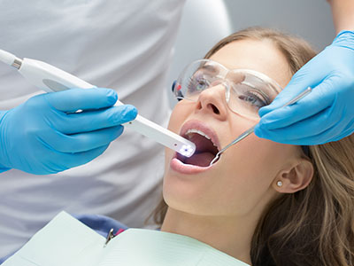 The image shows a dental professional using an oral care device on a patient s mouth while the patient is seated in a dental chair, wearing protective eyewear and a surgical mask.
