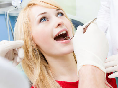 A woman receiving dental care with her mouth open while seated in a dentist's chair.