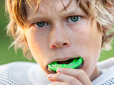 The image shows a young male with blonde hair, wearing a football uniform and holding a green object close to his mouth.