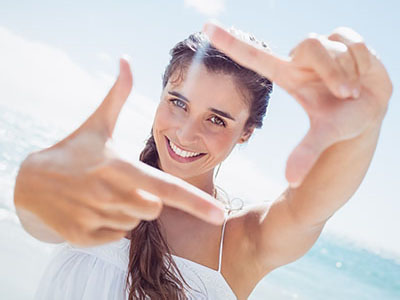 A woman taking a selfie with her hand against a sunny beach backdrop.