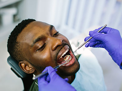 Alt text   A person receiving dental care, with a dentist performing work on their teeth while wearing gloves and a surgical mask.